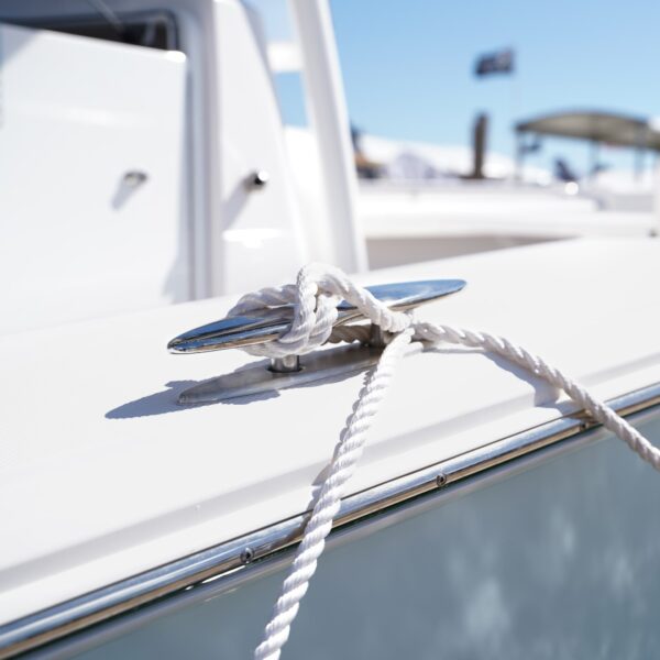 A stainless steel pull up cleat on the side of a boat with a white rope tied in a not around it.